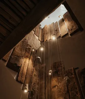 Beeindruckende Lichtinstallation mit schwebenden Steinen und massiven Altholzbohlen im Treppenhaus des eriro Alpine Hide – Kunst trifft alpine Architektur