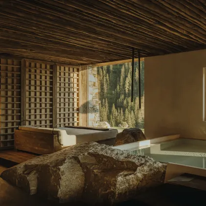eriro-Wellness mit Soaking-Pool, rohem Felsbrocken, Astholz-Deckengitter und Wetterstein-Panoramafenster durch japanische Holzlattentür