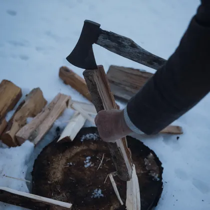 Axe splitting spruce wood on snow-covered chopping block at Wetterstein – fresh logs for fireside evening, alpine handcraft at eriro winter resort