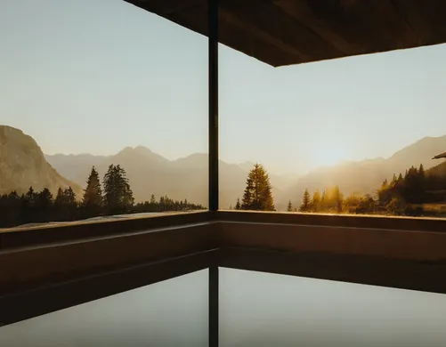 Infinity-Pool im eriro mit Überlaufkante zum Sonnenuntergang über Wetterstein- und Mieminger Kette, spiegelnde Wasserfläche unter dunkler Holzdecke