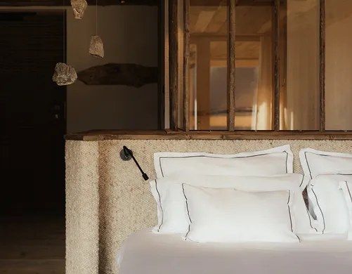 Luxuriöses Schlafzimmer im eriro Alpine Hide mit weißer Leinenbettwäsche, Wollkopfteil und schwebenden Kristallleuchten aus Naturstein