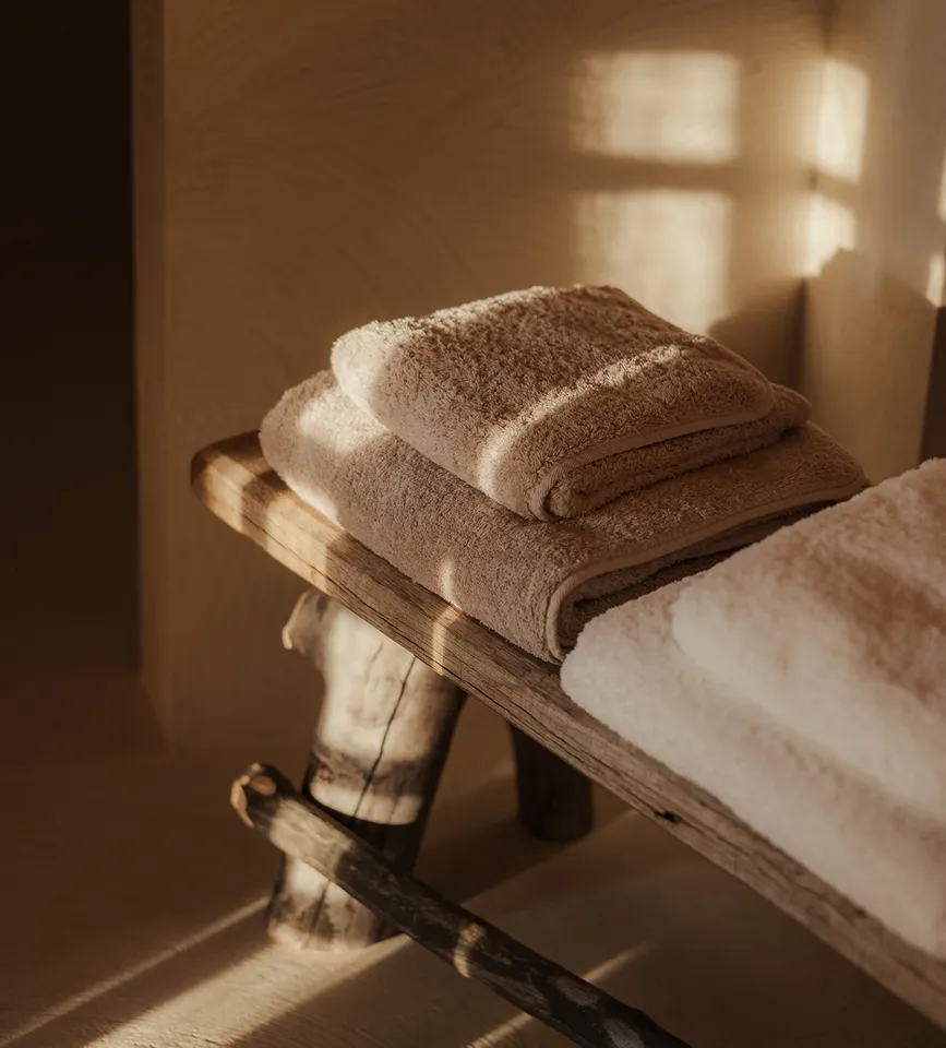 Weiche Handtücher in Taupe und Creme auf rustikaler Holzbank im warmen Licht – luxuriöse Spa-Geborgenheit im eriro Alpine Hide