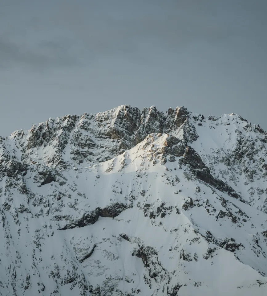 Schroffer Felsgipfel des Wettersteins unter Schnee und Eis, graue Wolken über zerklüftete Kalkstein-Grate – stille Erhabenheit der Berge bei eriro
